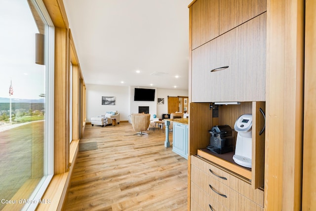 kitchen with open floor plan, recessed lighting, light wood-style floors, a warm lit fireplace, and modern cabinets
