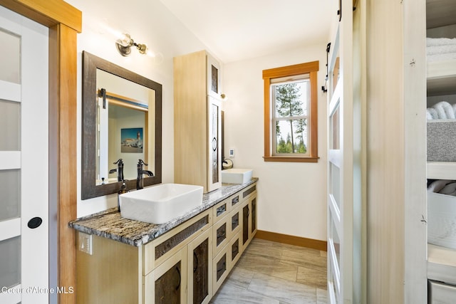 bathroom with baseboards, double vanity, and a sink
