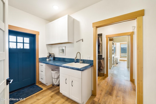 kitchen featuring dark countertops, white cabinets, light wood-type flooring, and a sink