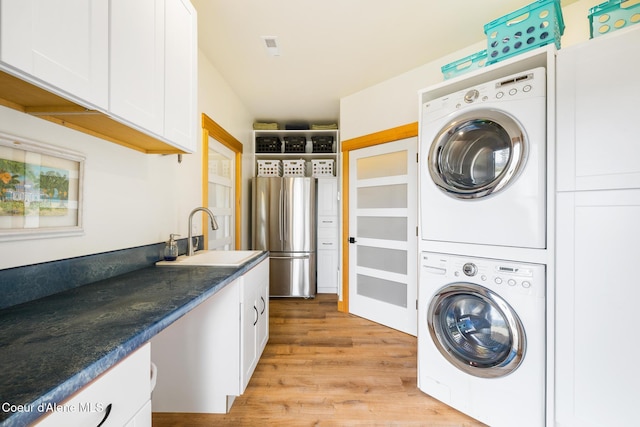 clothes washing area with a sink, cabinet space, stacked washer / drying machine, and light wood-type flooring