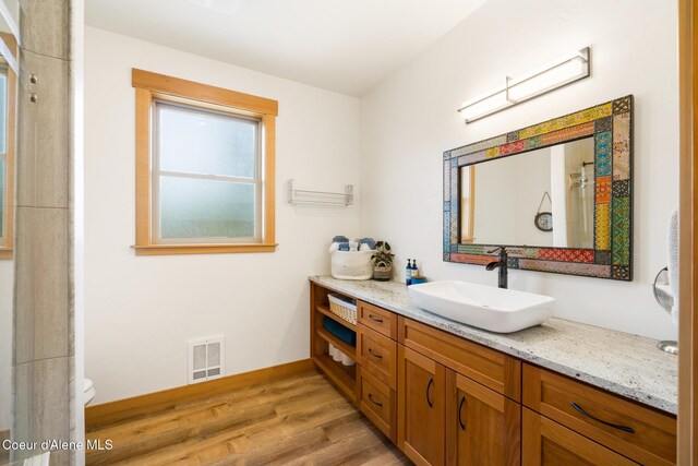 full bath featuring a shower, vanity, wood finished floors, baseboards, and visible vents