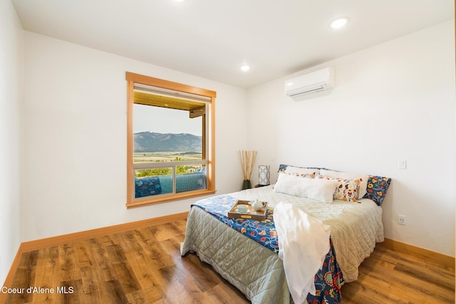 bedroom featuring a wall mounted air conditioner, baseboards, wood finished floors, and recessed lighting