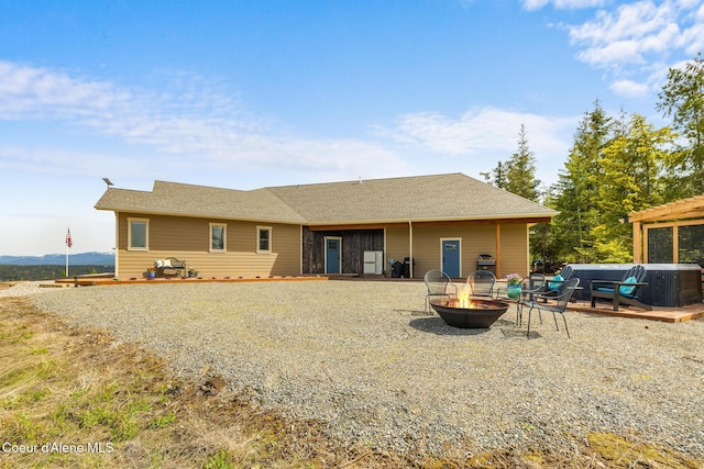 rear view of house with a hot tub, an outdoor fire pit, and roof with shingles