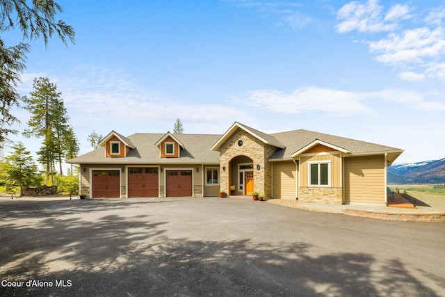 view of front facade featuring driveway, stone siding, a garage, and roof with shingles