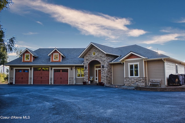 view of front of home featuring stone siding, a garage, driveway, and a shingled roof