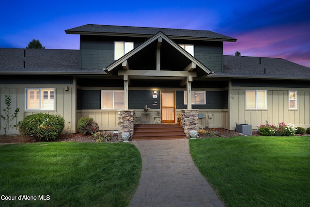 view of front of property with cooling unit, roof with shingles, board and batten siding, and a yard