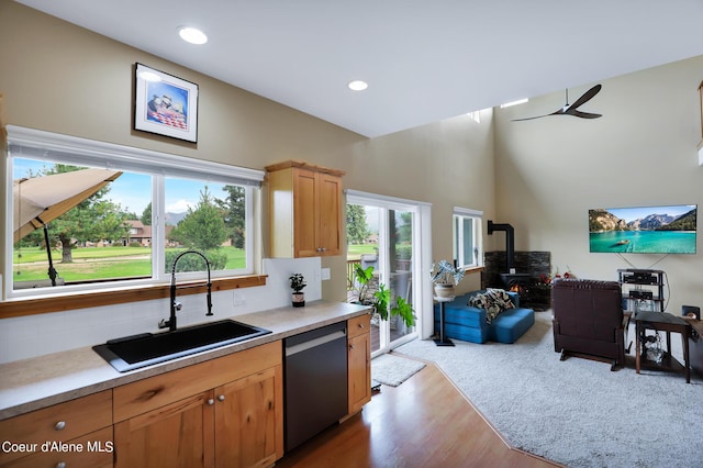 kitchen with a sink, wood finished floors, a wood stove, stainless steel dishwasher, and ceiling fan