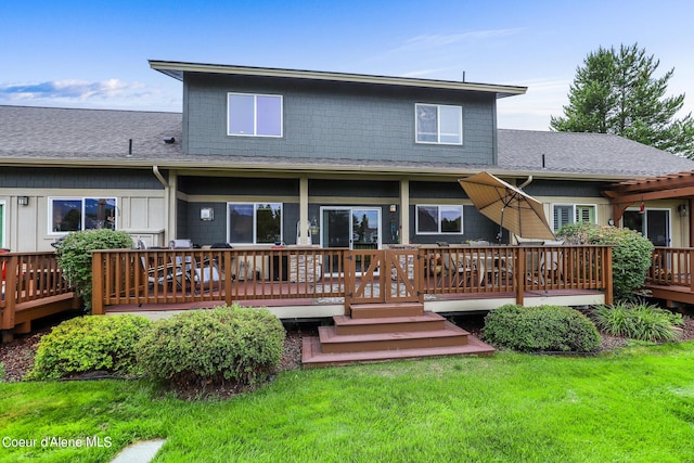 rear view of property featuring a shingled roof, a deck, and a yard