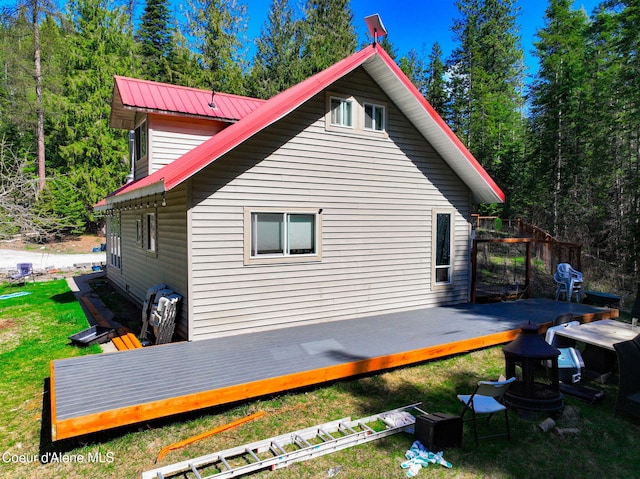 view of property exterior with a deck, a yard, metal roof, and a view of trees