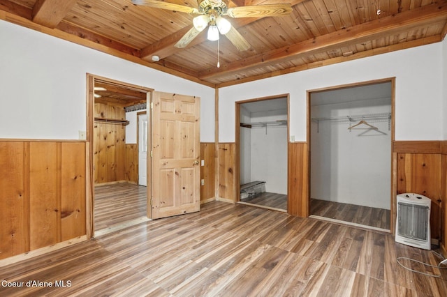 unfurnished bedroom with beamed ceiling, wainscoting, two closets, and wood ceiling
