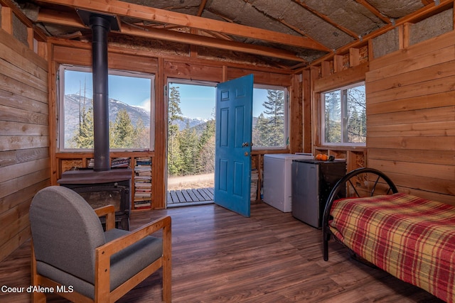 bedroom with refrigerator, wood walls, a wood stove, and wood finished floors