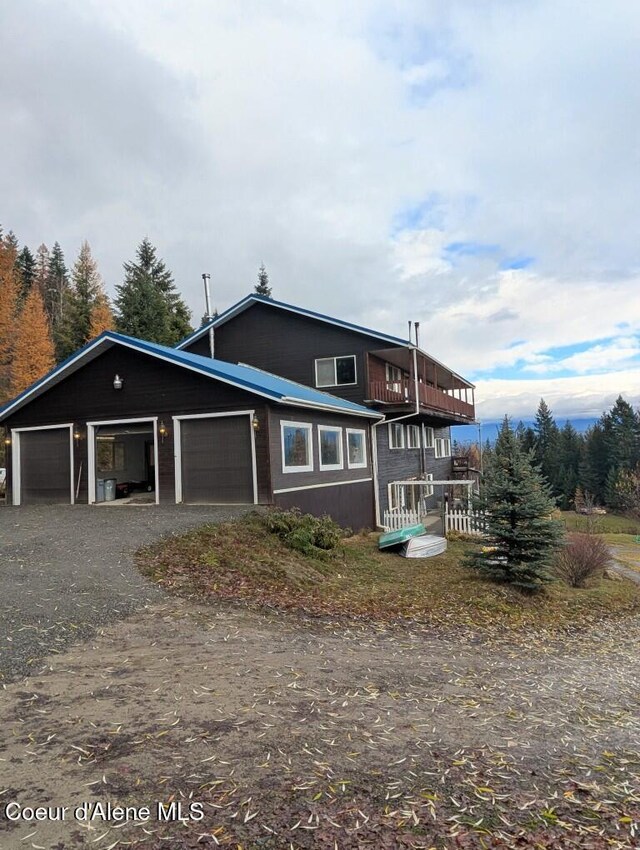 view of front of home with dirt driveway, a balcony, and a garage