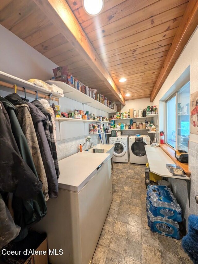 laundry area with laundry area, stone finish floor, wood ceiling, washing machine and clothes dryer, and a sink