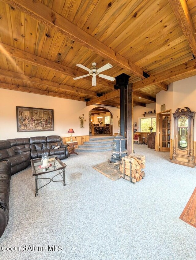 living room featuring carpet flooring, arched walkways, beamed ceiling, and a wood stove
