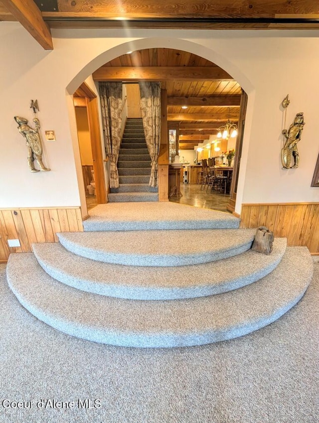 stairway featuring wood ceiling, wood walls, beam ceiling, a wainscoted wall, and carpet