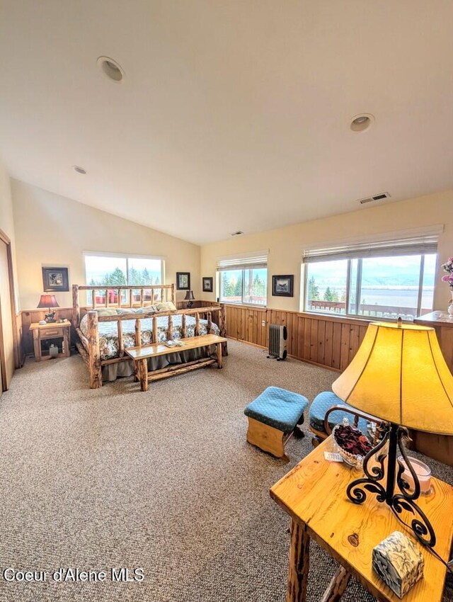 carpeted bedroom with wainscoting, vaulted ceiling, wooden walls, and visible vents