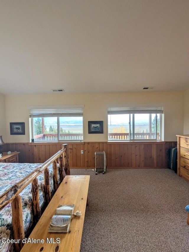 bedroom featuring visible vents, carpet floors, wainscoting, radiator heating unit, and multiple windows