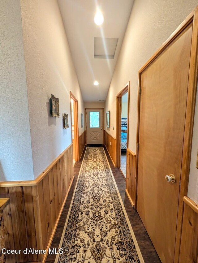 hall featuring wooden walls, dark wood-style flooring, vaulted ceiling, and wainscoting