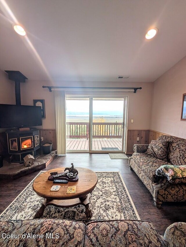 living area with visible vents, a wood stove, wood finished floors, a wainscoted wall, and wooden walls