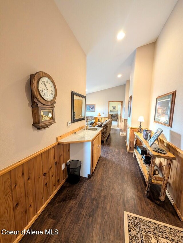 hall featuring wooden walls, dark wood-style flooring, vaulted ceiling, and wainscoting
