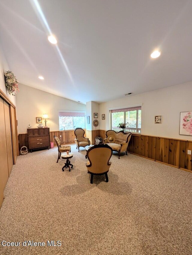 carpeted living room with wood walls, wainscoting, and lofted ceiling