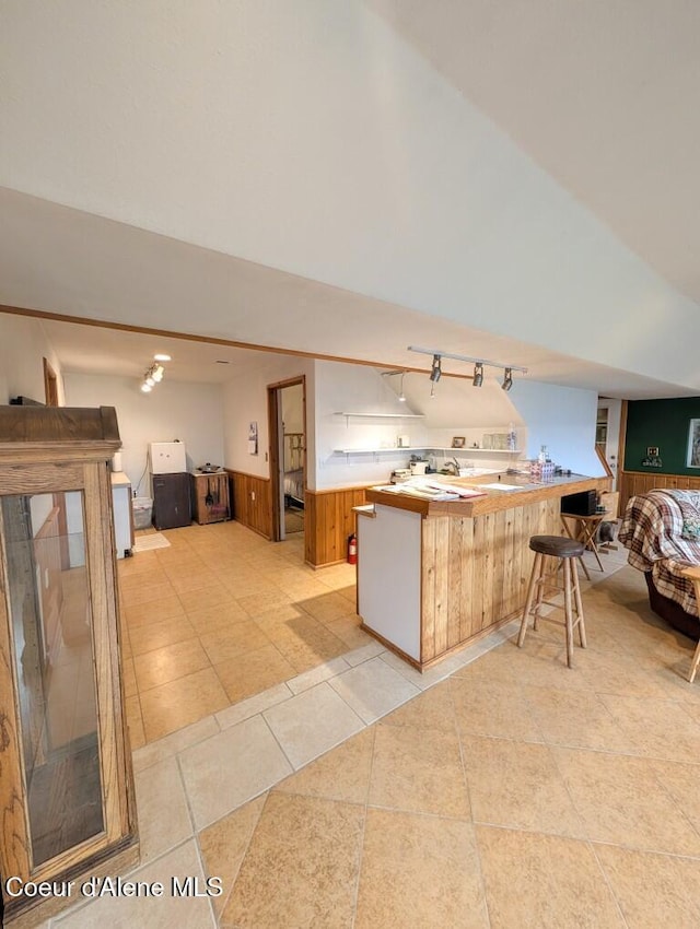kitchen featuring a peninsula, open floor plan, a kitchen breakfast bar, light countertops, and a wainscoted wall
