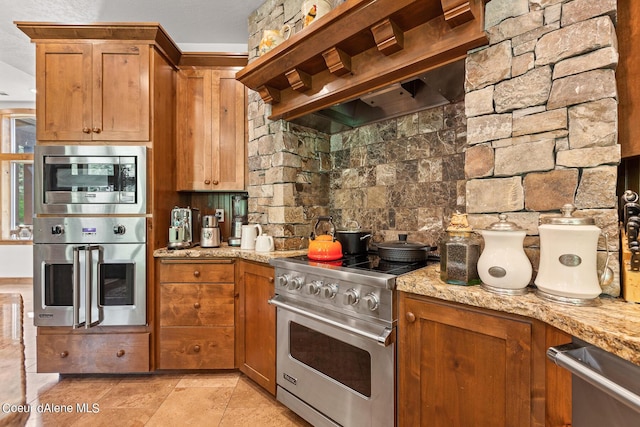 1990 S Gateway Ranch Rd, Coeur Dalene, ID 83814 - kitchen featuring wall chimney range hood, light stone countertops, brown cabinets, and appliances with stainless steel finishes
