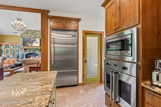 1990 S Gateway Ranch Rd, Coeur Dalene, ID 83814 - kitchen with an inviting chandelier, built in appliances, a fireplace, brown cabinetry, and light stone counters
