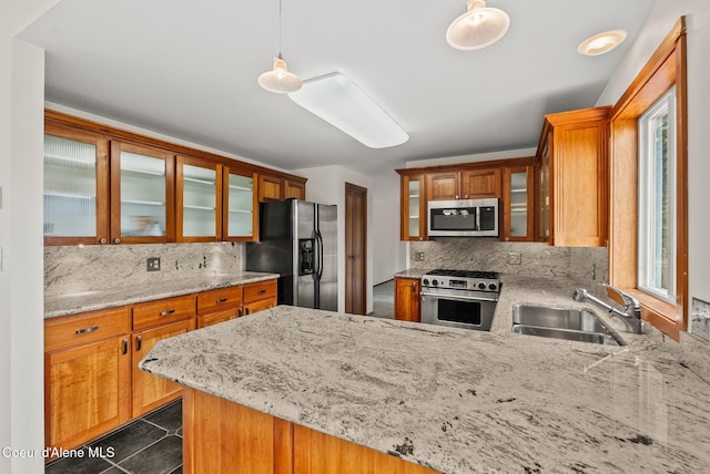 kitchen with tasteful backsplash, a sink, appliances with stainless steel finishes, a peninsula, and light stone countertops