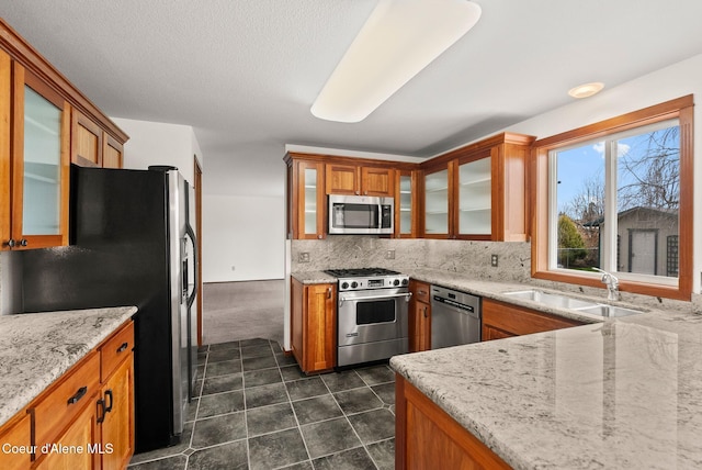 kitchen with backsplash, light stone countertops, brown cabinets, stainless steel appliances, and a sink