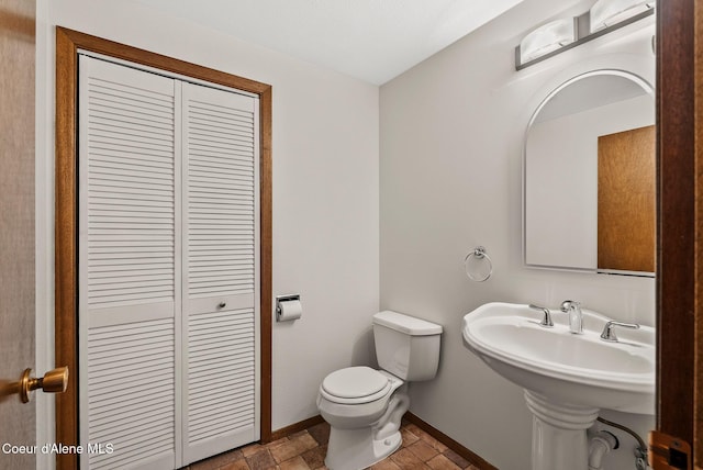 bathroom with a closet, baseboards, toilet, stone finish flooring, and a sink