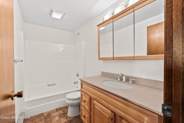 bathroom with stone finish flooring, washtub / shower combination, vanity, and toilet