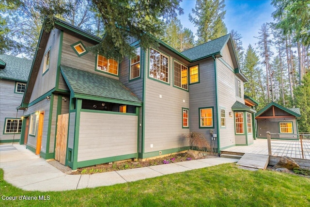 view of front of home featuring roof with shingles, a wooden deck, and a front lawn