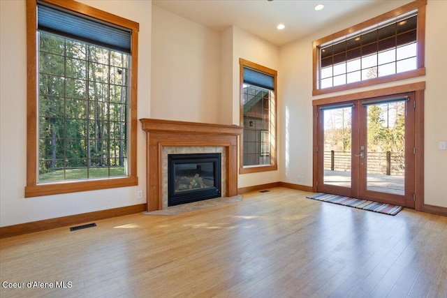 unfurnished living room with a fireplace, visible vents, wood finished floors, french doors, and baseboards