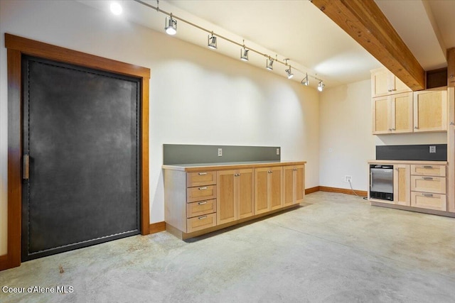 kitchen featuring concrete floors, baseboards, track lighting, beam ceiling, and light brown cabinetry