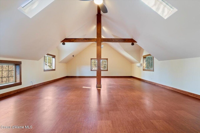 additional living space with vaulted ceiling with skylight, wood finished floors, baseboards, and a ceiling fan