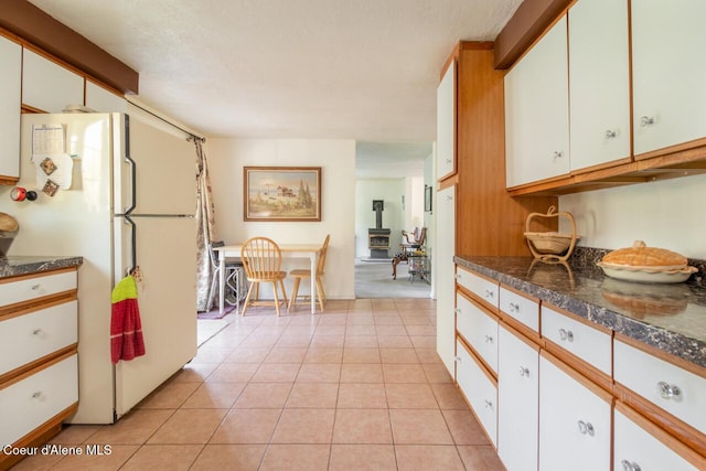 kitchen with freestanding refrigerator, dark countertops, light tile patterned floors, and white cabinets