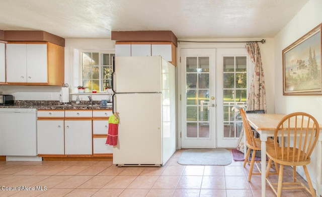 kitchen with a sink, white appliances, french doors, light tile patterned floors, and white cabinets