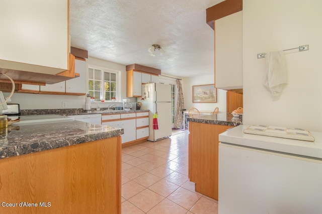 kitchen featuring light tile patterned floors, white appliances, a sink, dark stone counters, and white cabinets