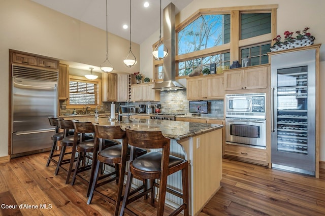 3765 Bottle Bay Rd, Sagle, ID 83860 - kitchen featuring built in appliances, ventilation hood, light brown cabinetry, a center island with sink, and wood-type flooring