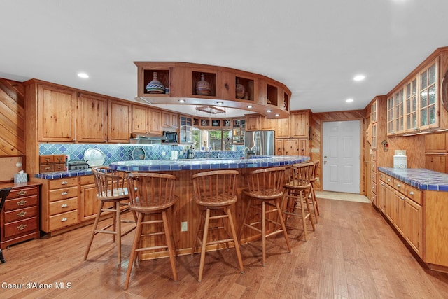 kitchen with glass insert cabinets, a breakfast bar area, recessed lighting, stainless steel fridge with ice dispenser, and light wood-style flooring