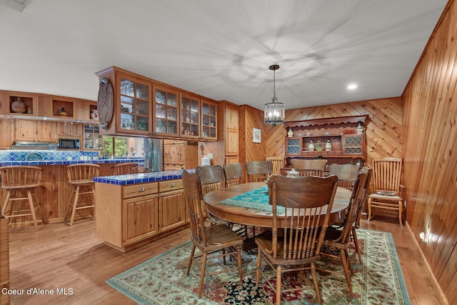 dining space with wooden walls, recessed lighting, light wood finished floors, and a notable chandelier