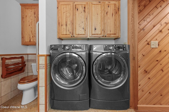 clothes washing area featuring wainscoting, tile patterned floors, tile walls, and washing machine and dryer