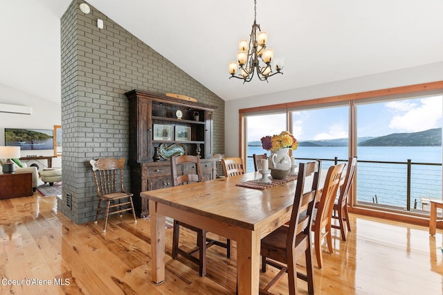 dining space featuring a water view, light wood finished floors, an inviting chandelier, and lofted ceiling