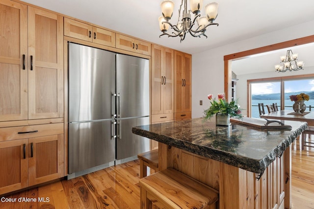 kitchen featuring high end fridge, an inviting chandelier, light wood-style flooring, a breakfast bar area, and hanging light fixtures