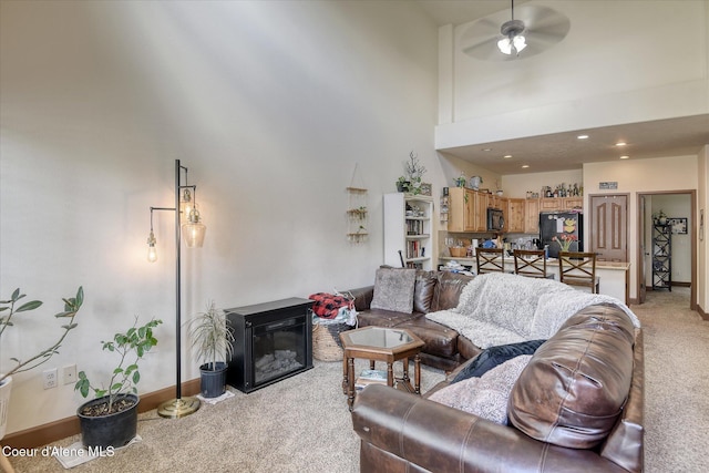living room with light carpet, a high ceiling, a glass covered fireplace, baseboards, and a ceiling fan