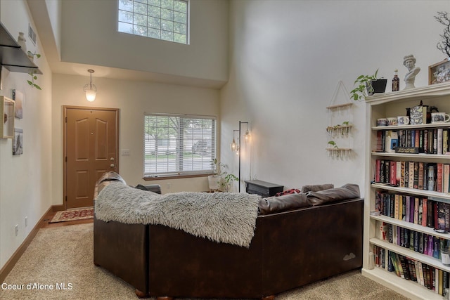 living area featuring a towering ceiling, light colored carpet, and baseboards