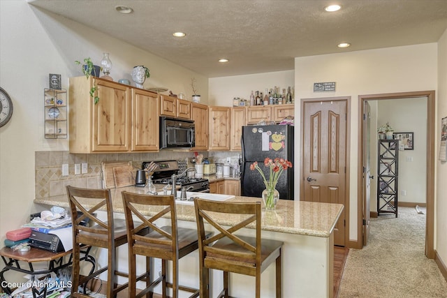 kitchen featuring black appliances, backsplash, light stone counters, recessed lighting, and a peninsula