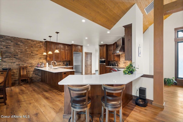kitchen with light wood-type flooring, wall chimney range hood, a peninsula, decorative backsplash, and a sink