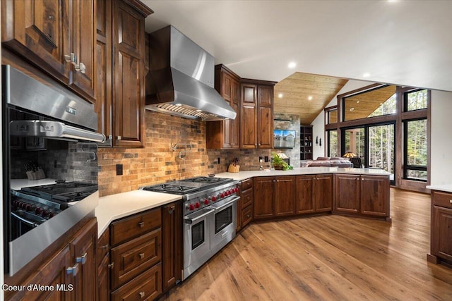 kitchen with wall chimney range hood, a peninsula, light countertops, lofted ceiling, and appliances with stainless steel finishes